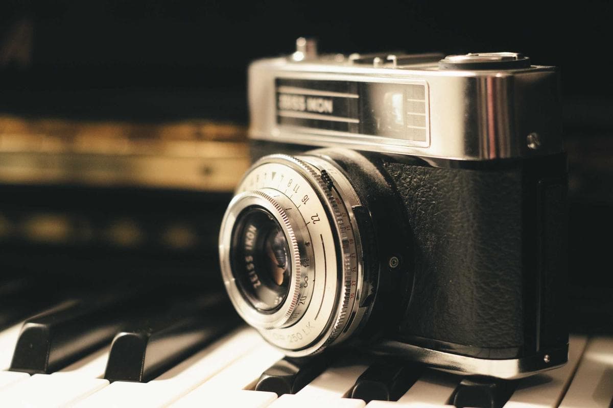 A silver and black vintage rangefinder camera resting on piano keys.